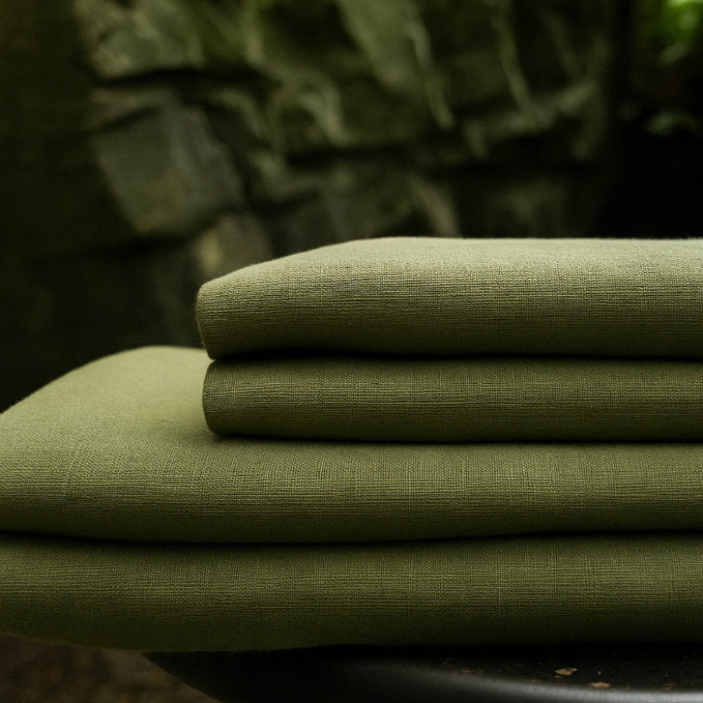 Stack of folded green linen bedding, showing a 4 piece sheet set