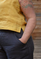 Person wearing a yellow top and dark grey linen pants with a wooden background