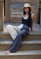 A woman sitting on wooden steps wearing two-toned linen lounge pants. One leg is dark grey, the other is light beige.