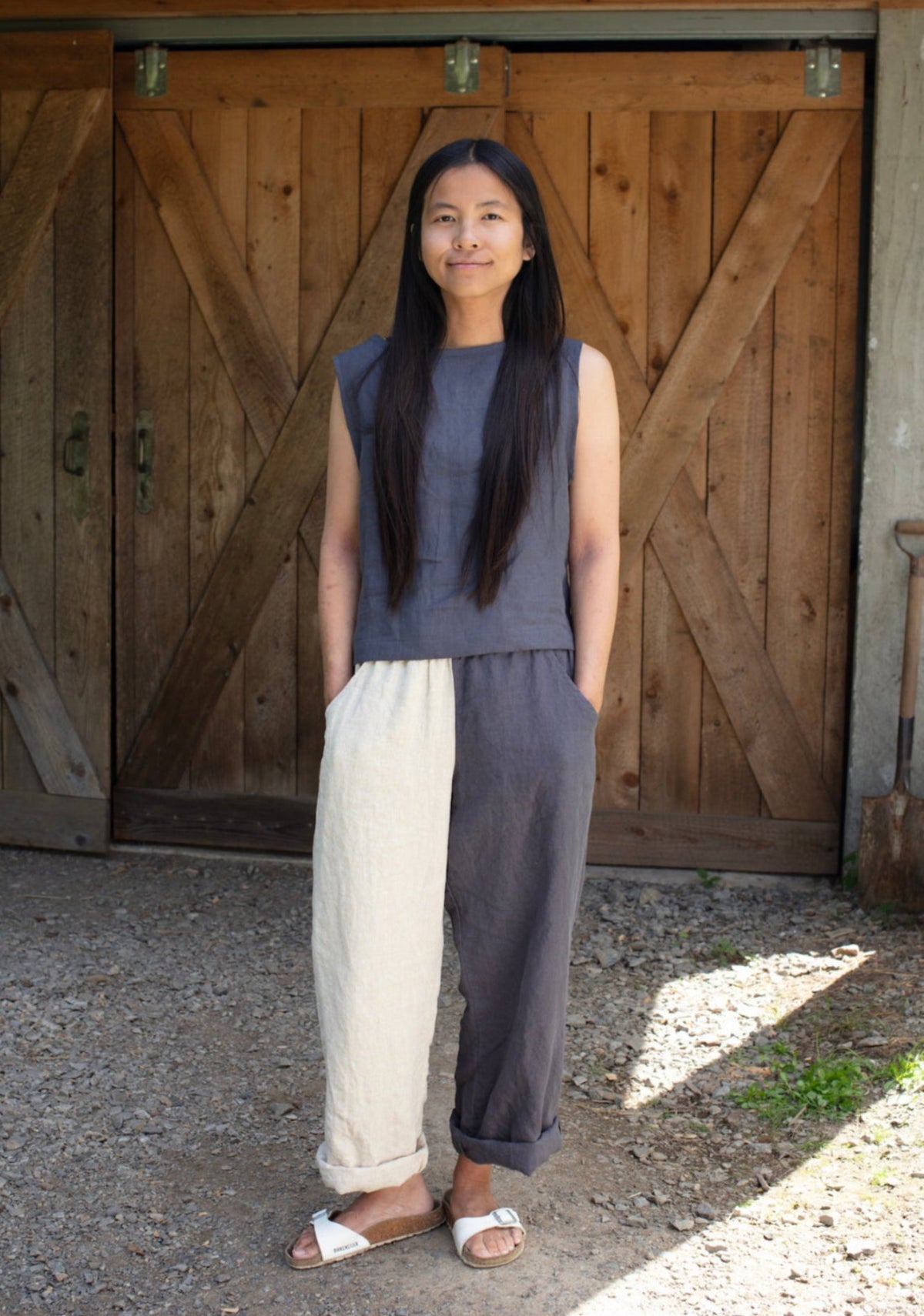 Woman standing in front of a wooden door wearing a sleeveless top and two-tone linen pants.