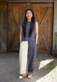 Woman standing in front of a wooden door wearing a sleeveless top and two-tone linen pants.